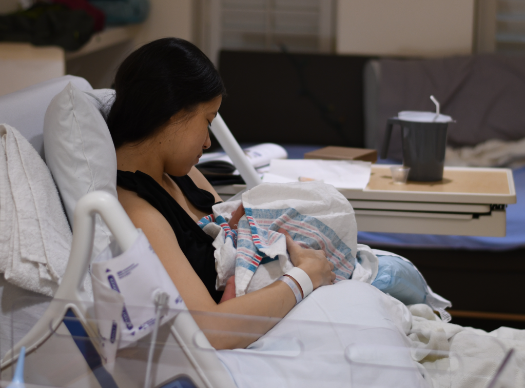 Woman holding newborn baby, sitting in hospital bed.